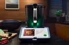 Immagine del nuovo Bimby TM7 con display touchscreen HD e ricetta di Pad Thai, circondato da ingredienti freschi come lime, zenzero e peperoncini, su un tavolo moderno.